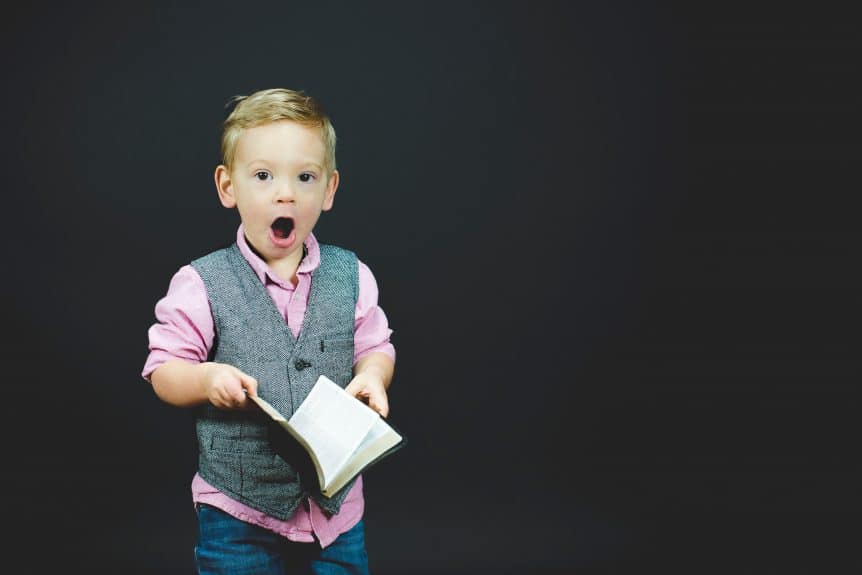 small boy holding book with shocked expression